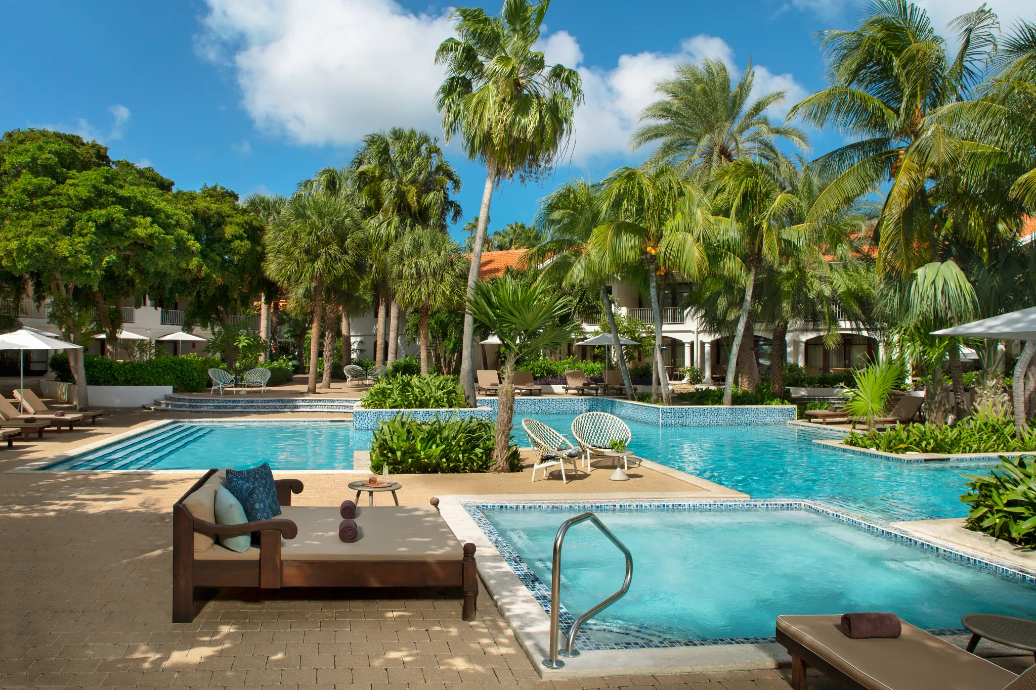Tranquil swimming pool surrounded by palm trees and loungers at Zoëtry Curaçao Resort & Spa, designed for relaxation and wellness.